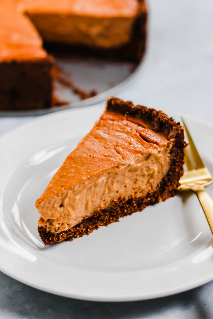 a slice of vegan pumpkin cheesecake served on a white plate with a gold fork