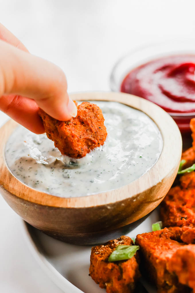 a vegan tofu nugget being dipped into a cup of dairy free ranch
