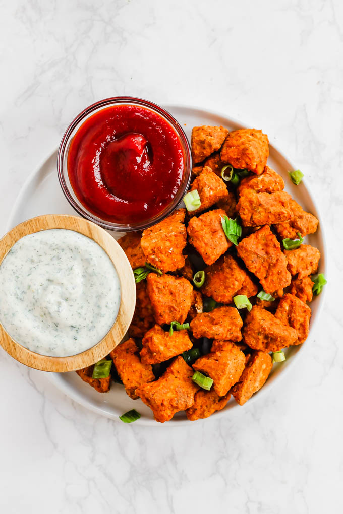 a plate of baked tofu nuggets served with ketchup and vegan ranch