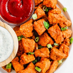 A plate of vegan nuggets served with a bowl of ketchup and a bowl of vegan ranch