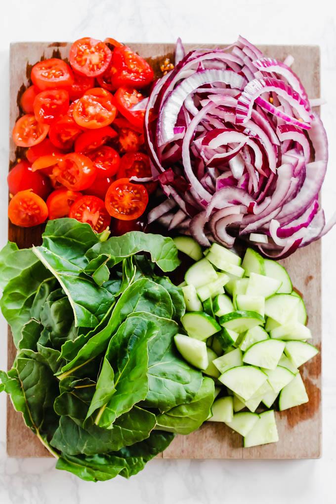 a cutting board serving chopped tomatoes, sliced red onion, diced tomatoes and fresh greens