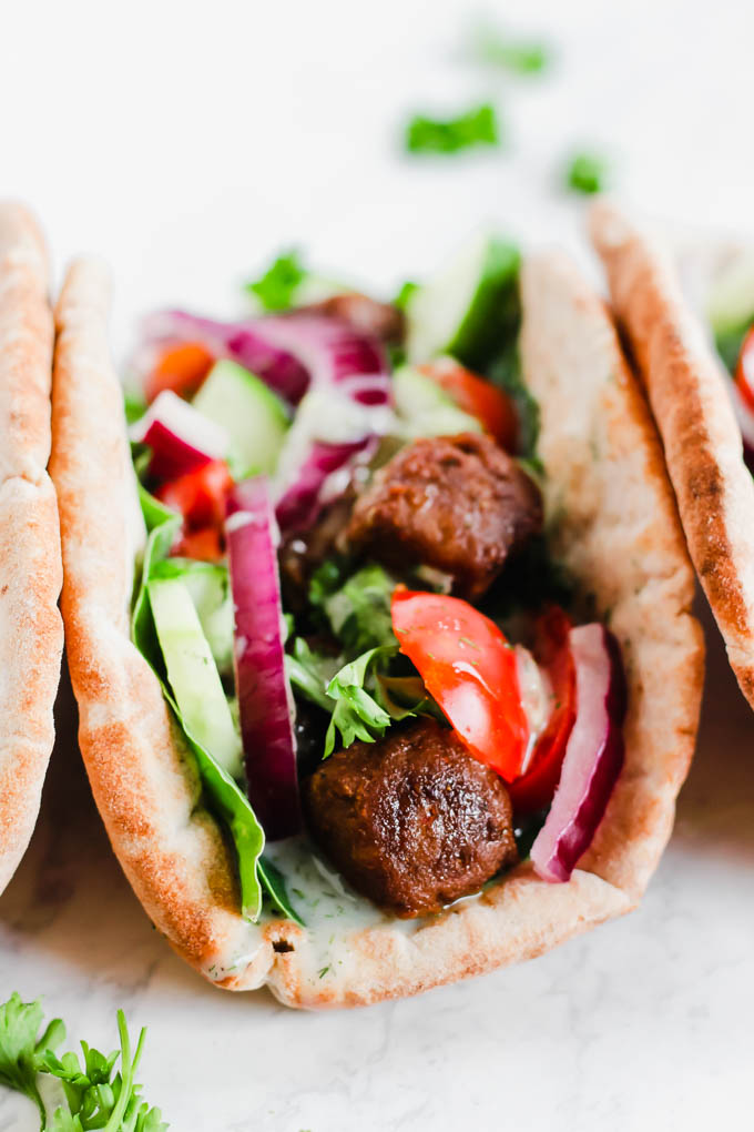 a close up of a pita stuffed with vegan beef, fresh vegetables and tzatziki