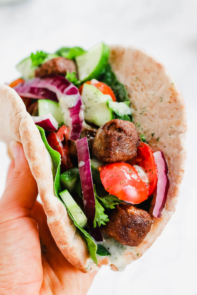 a hand holding a vegan gyro topped with greens, red onion and tzatziki
