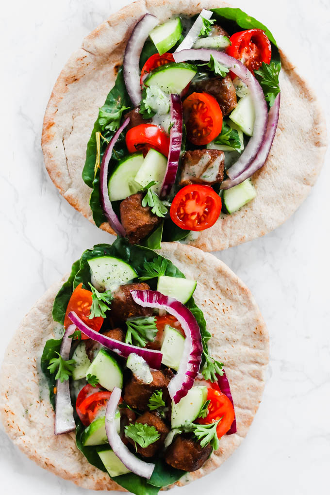two pitas topped with fresh greens, cucumber, red onion, tomatoes and vegan beef