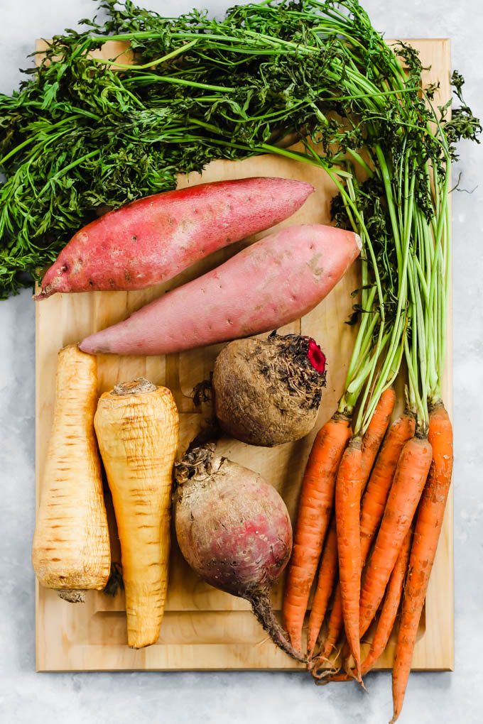 a bunch of carrots, two beets, two sweet potatoes and two parsnips on a cutting board