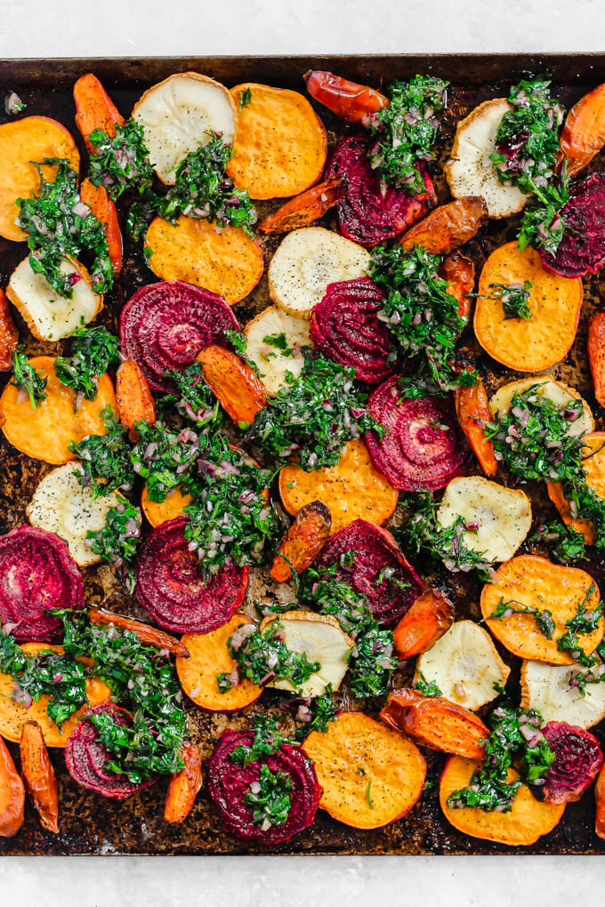 a tray of roasted vegetables with a carrot top chimichurri