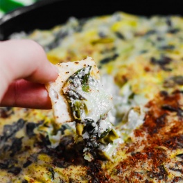 a chip being dipped into a vegan spinach artichoke dip