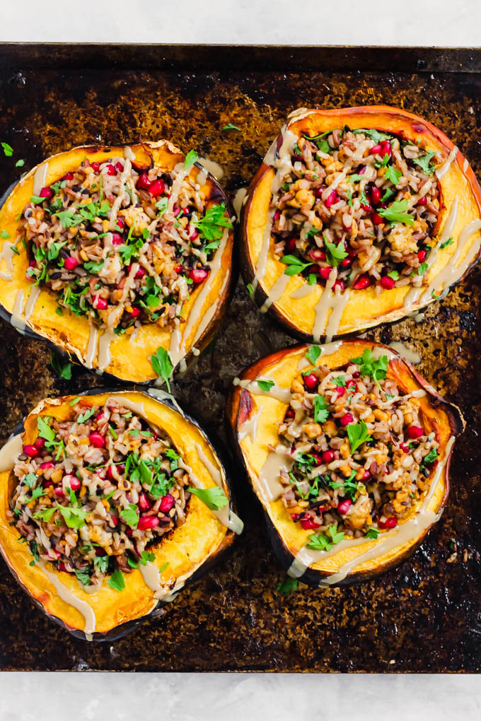 four halves of acorn squashes stuffed with wild rice, tempeh, pomegranate seeds and topped off with fresh cilantro and tahini