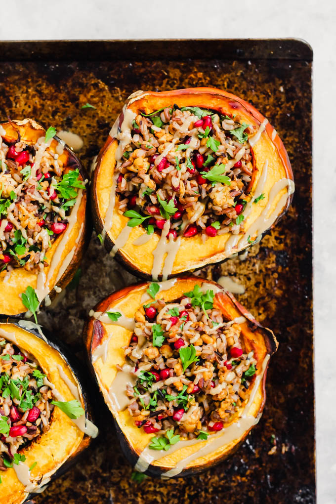 four halves of acorn squashes, each filled with a wild rice and tempeh stuffing and topped with fresh cilantro and a drizzle of tahini