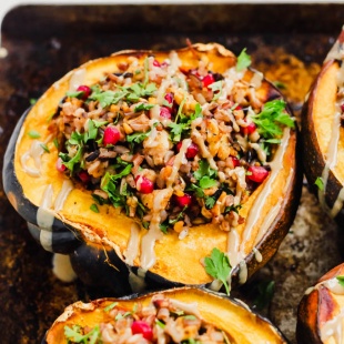 halved acorn squashes on a cookie sheet filled with a tempeh wild rice stuffing and topped with tahini