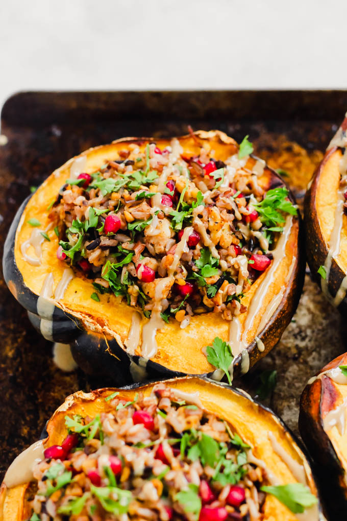 halved acorn squashes on a cookie sheet filled with a tempeh wild rice stuffing and topped with tahini