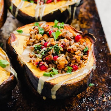 a close up shot of a stuffed acorn squash filled with wild rice, tempeh and pomegranate seeds