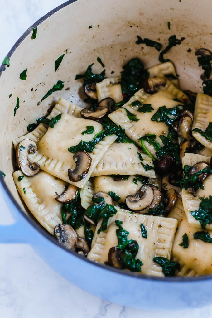 a pot filled with vegan ravioli being sauteed with greens and sliced mushrooms