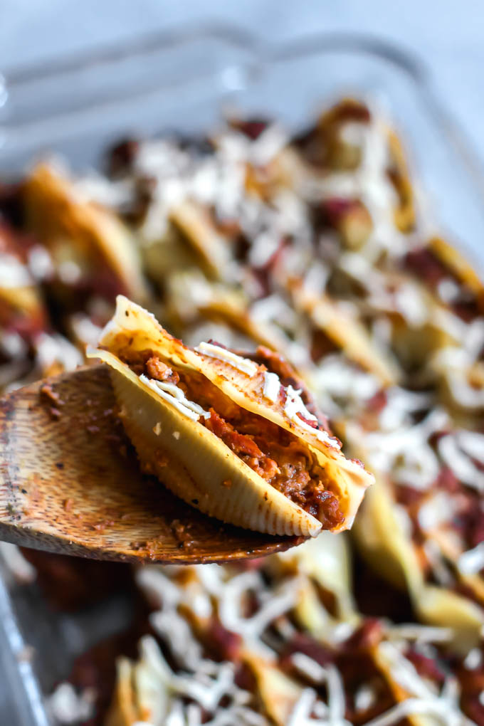 a wooden spoon scooping out a serving of stuffed shells