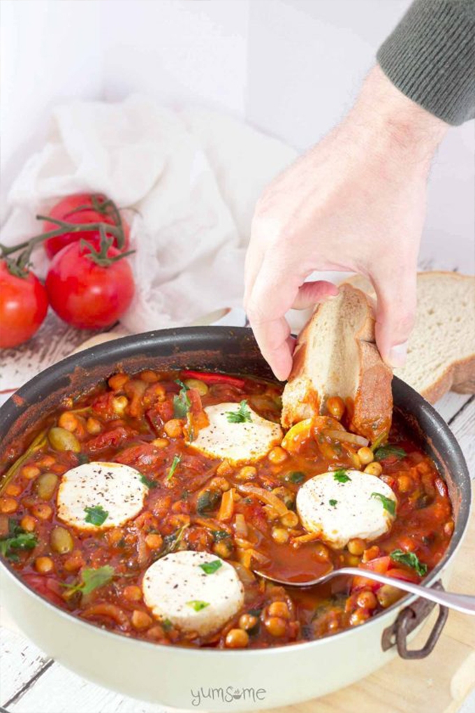 A hand scoops a piece of bread into a pot of vegan shakshuka