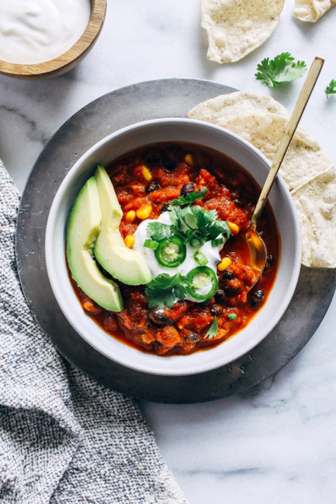 Vegan pumpkin chili topped with two slices of avocado, vegan sour cream, jalapenos and cilantro