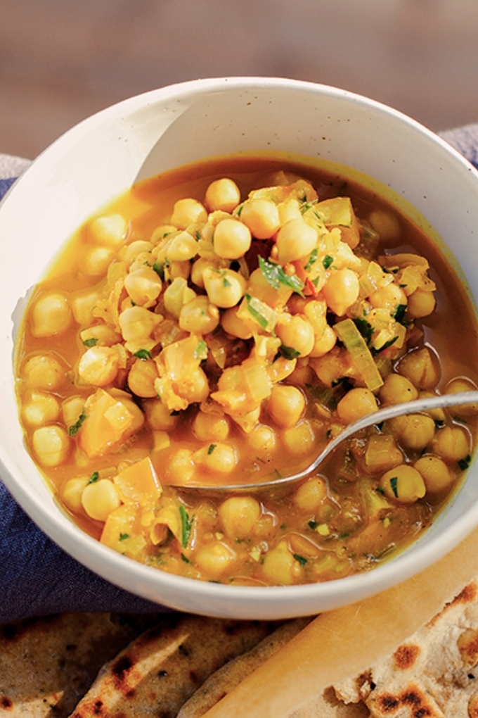 A spoon taking a scoop of golden chana masala out of a white bowl