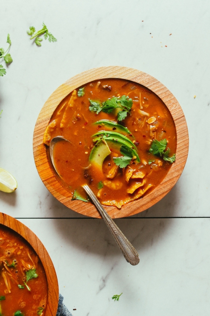 A wooden bowl filled with vegan taco soup topped with cilantro and avocado slices