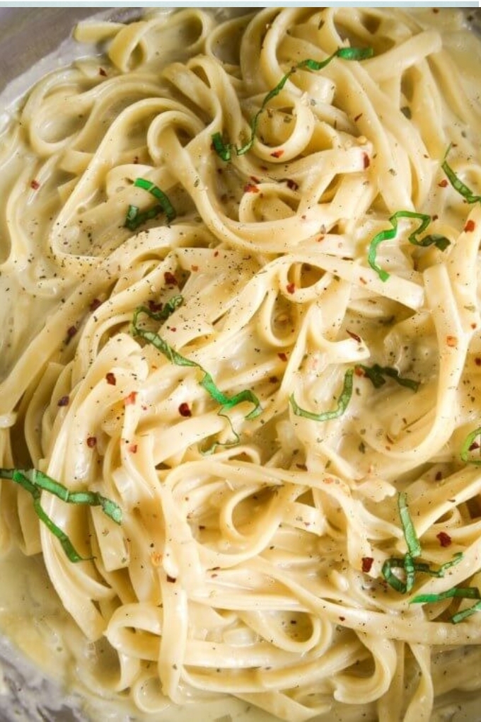 A creamy pot of vegan fettuccini pasta topped with ribbons of basil and red pepper flakes