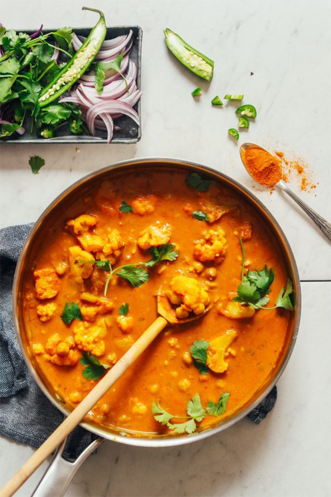 A pot of yellow chickpea coconut curry served alongside a platter of green chilis, red onion and cilantro