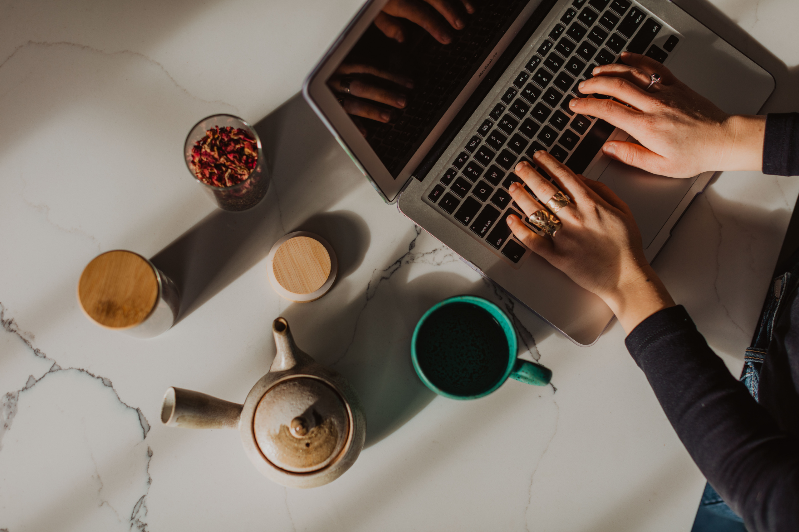 hands typing on a laptop with a teapot and a mug of tea