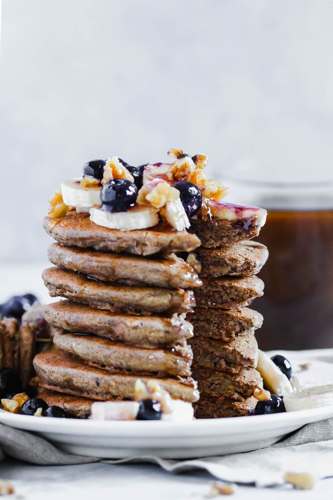 A stack of buckwheat pancakes topped with bananas, blueberries, chopped walnuts and maple syrup