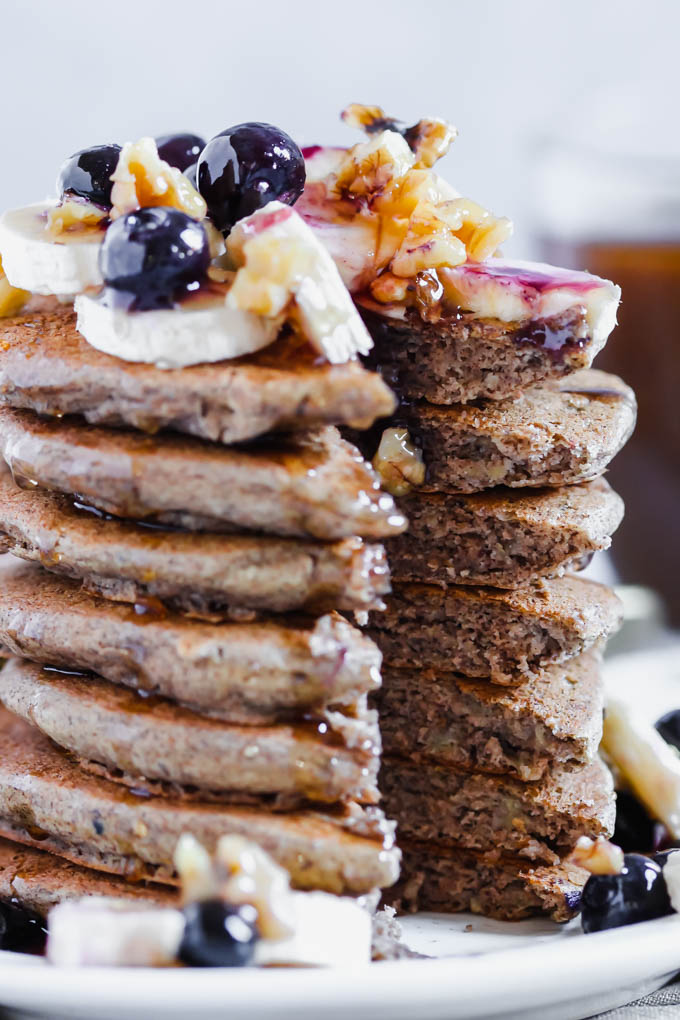 A tall stack of vegan pancakes topped with bananas, blueberries and walnuts