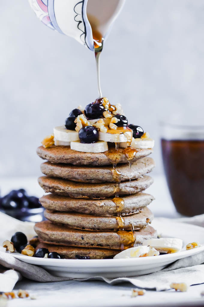Maple syrup is poured on top of a stack of pancakes