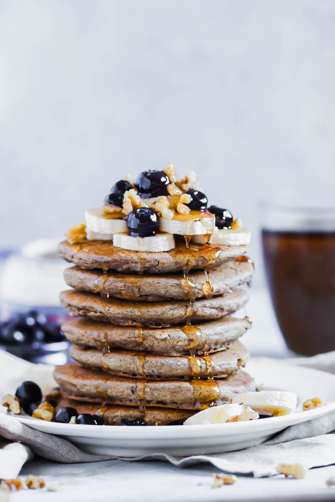 A plate of pancakes topped with bananas, blueberries, walnuts and syrup served with a cup of coffee
