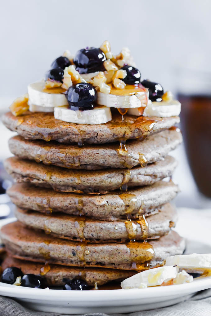 A pile of vegan pancakes served with fresh fruit, nuts and maple syrup