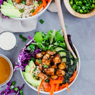 a lunch bowl filled with tofu, greens, cabbage, cucumber, avocado, carrots and nori