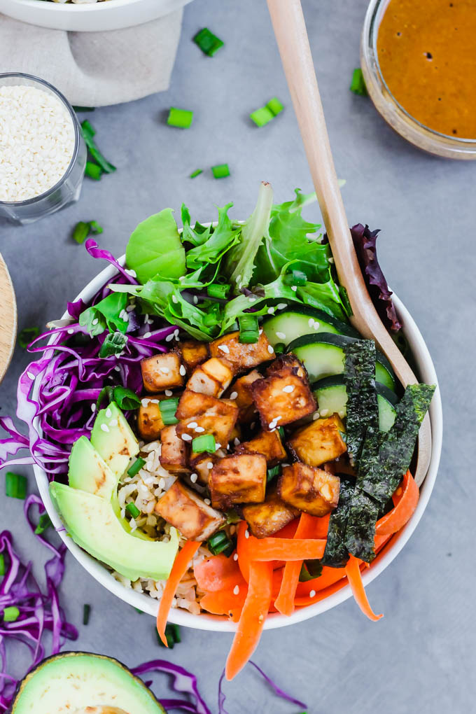 a vegan poke bowl filled with vegetables and roasted tofu