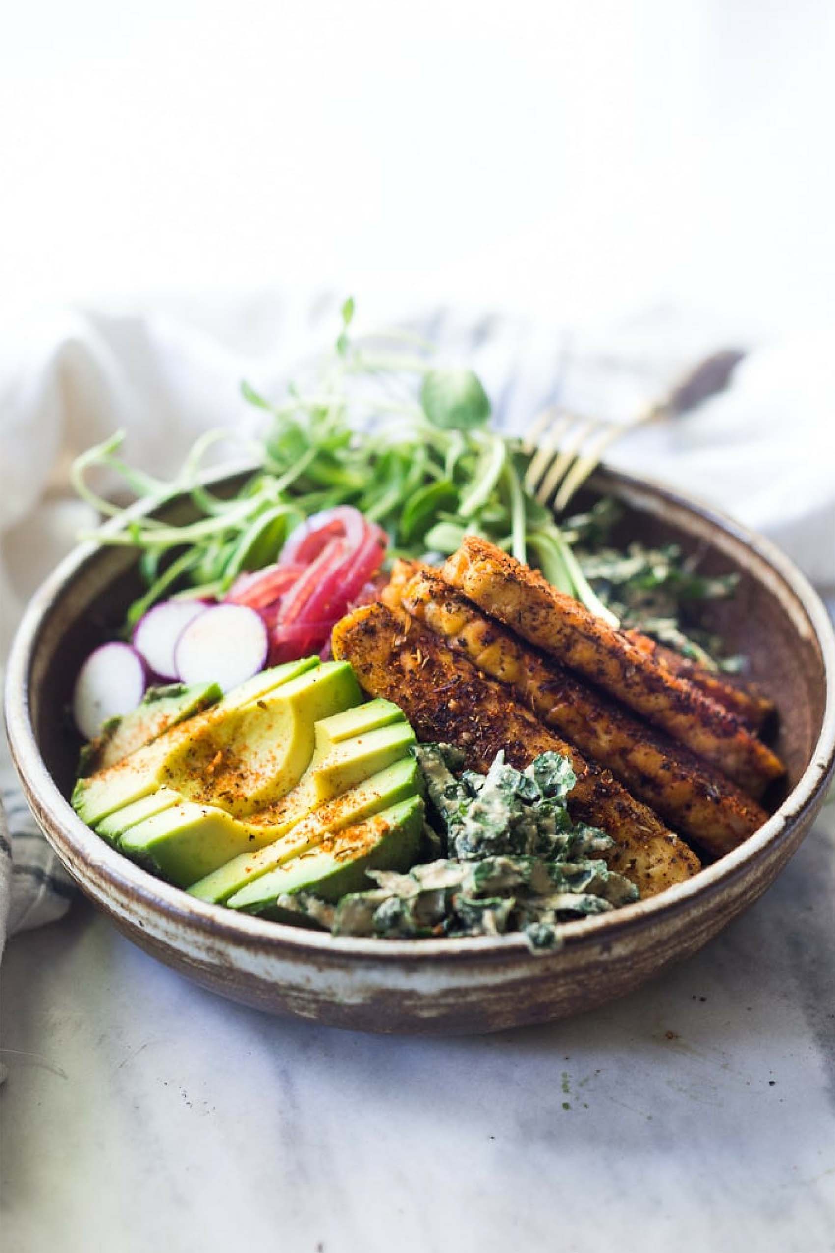 a kale salad topped with fried sliced tempeh and avocado