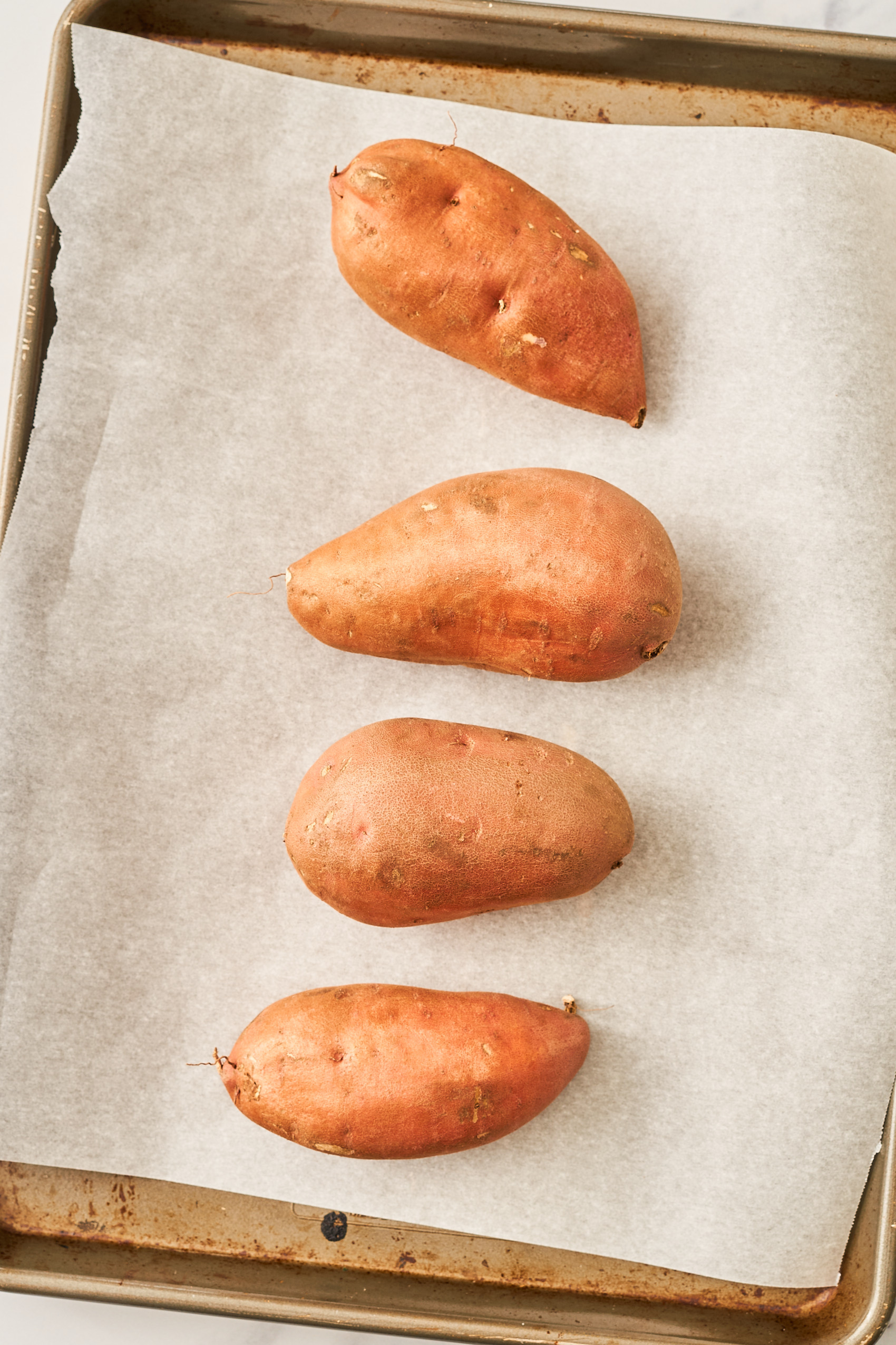 four whole sweet potatoes on a baking sheet lined with parchment paper before being baked