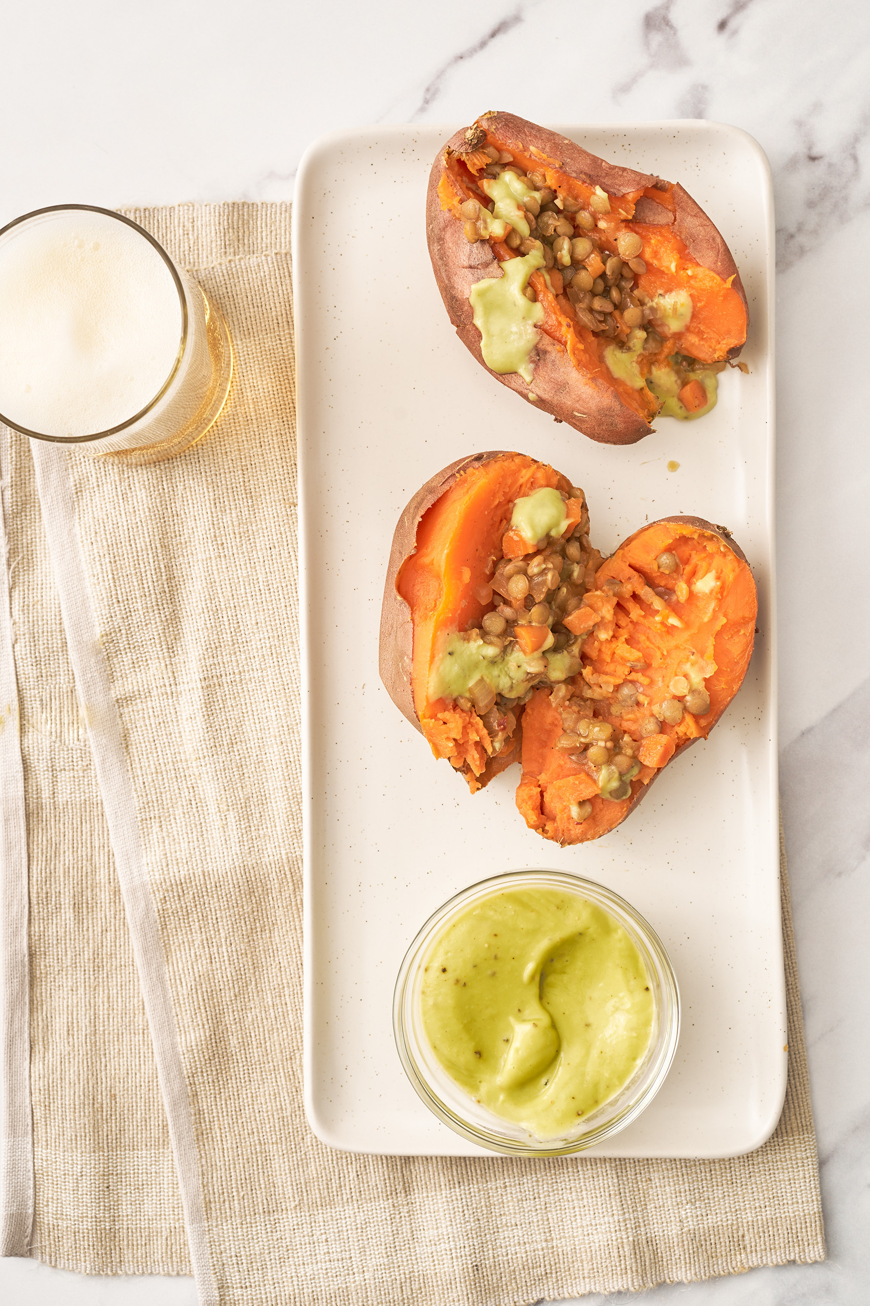 two sweet potatoes sliced in half and topped with barbecue lentils and a creamy avocado sauce