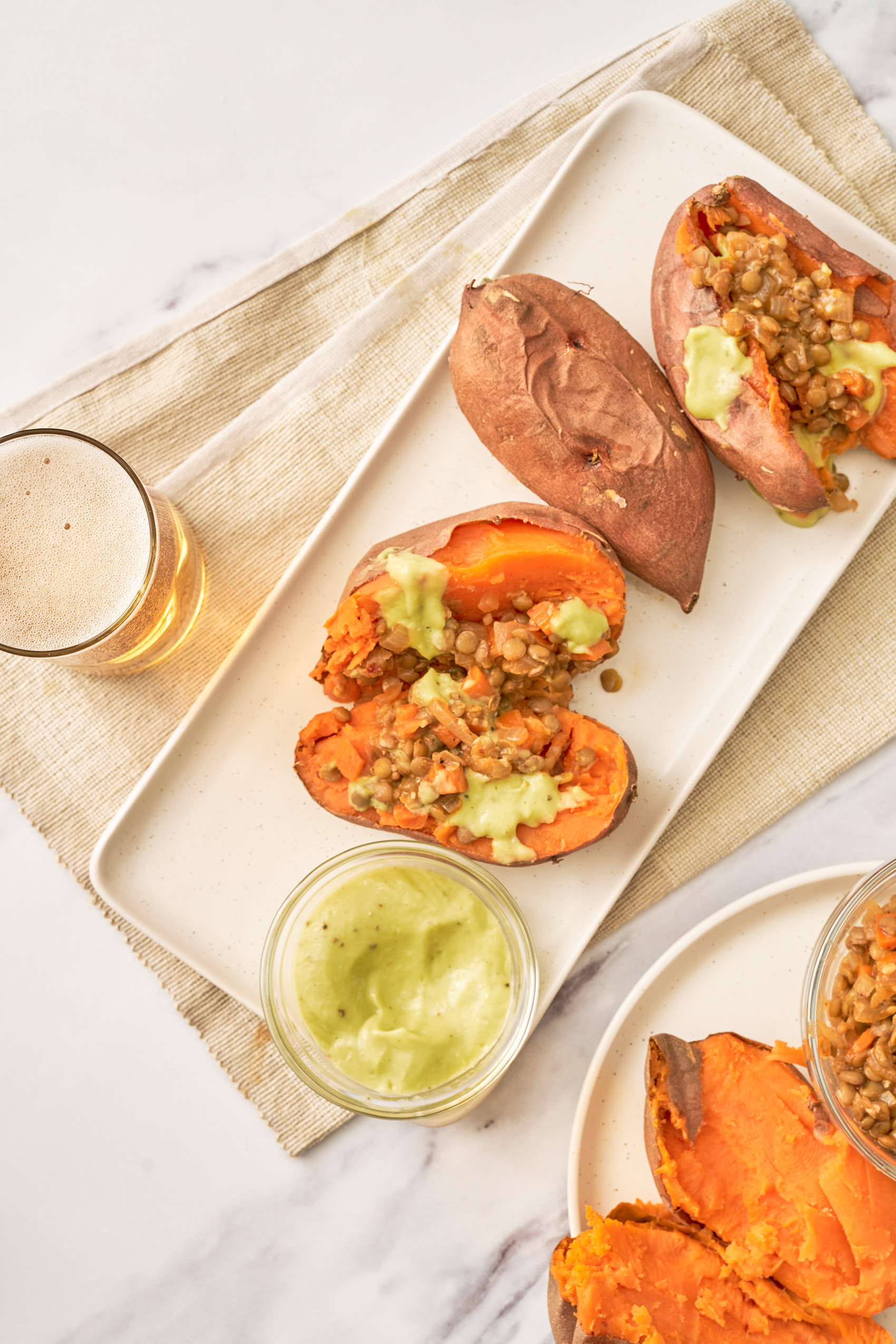 two sweet potatoes that have been sliced down the middle and stuffed with lentils, served with an avocado sauce