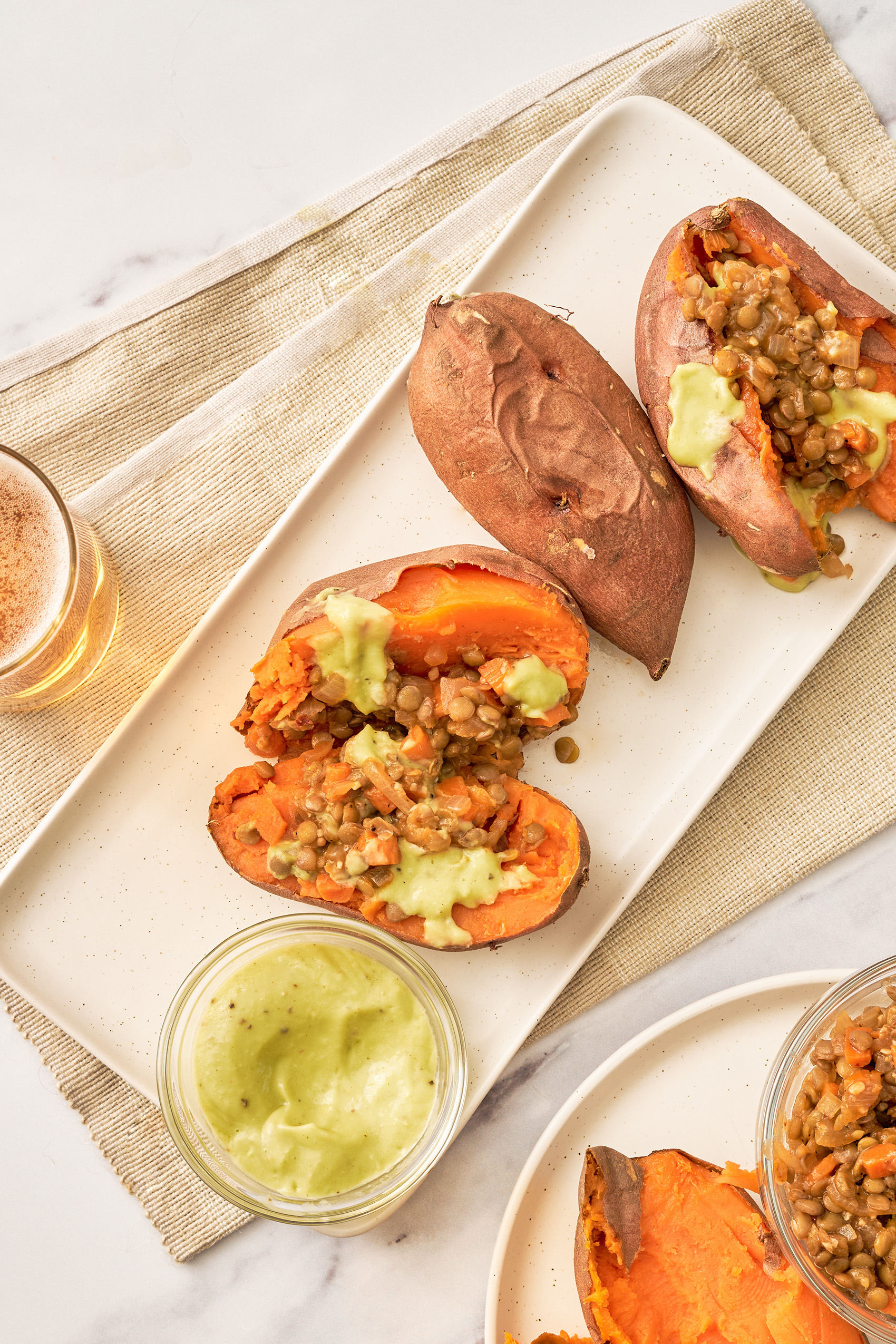 three sweet potatoes, one whole and two sliced in half and stuffed with lentils and avocado sauce