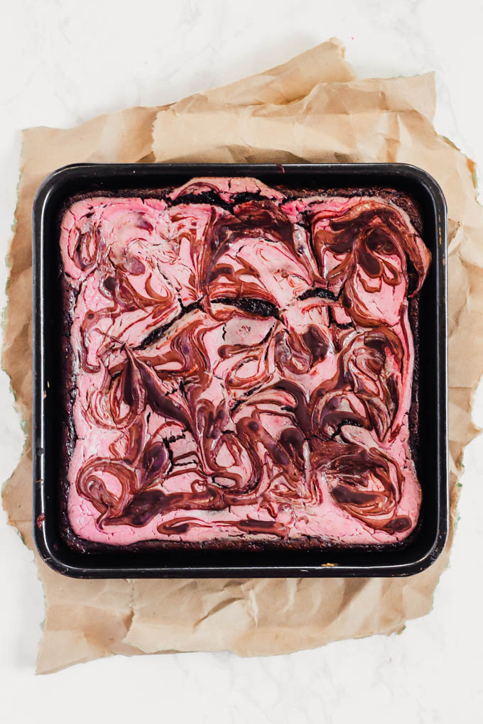 a pan of vegan brownies topped with a strawberry cheesecake swirl