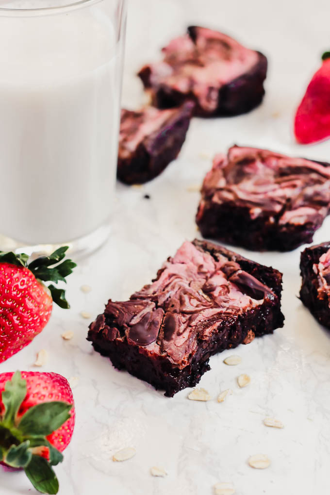 a glass of plant-based milk served next to a batch of strawberry cheesecake brownies