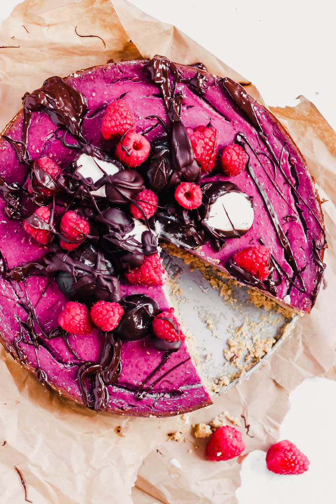 a whole raspberry cheesecake topped with drizzled chocolate and fresh raspberries