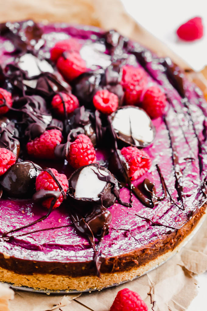 a whole vegan raspberry cheesecake topped with fresh berries and chocoalte