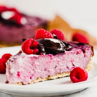 a slice of vegan raspberry cheesecake topped with chocolate and fresh raspberries
