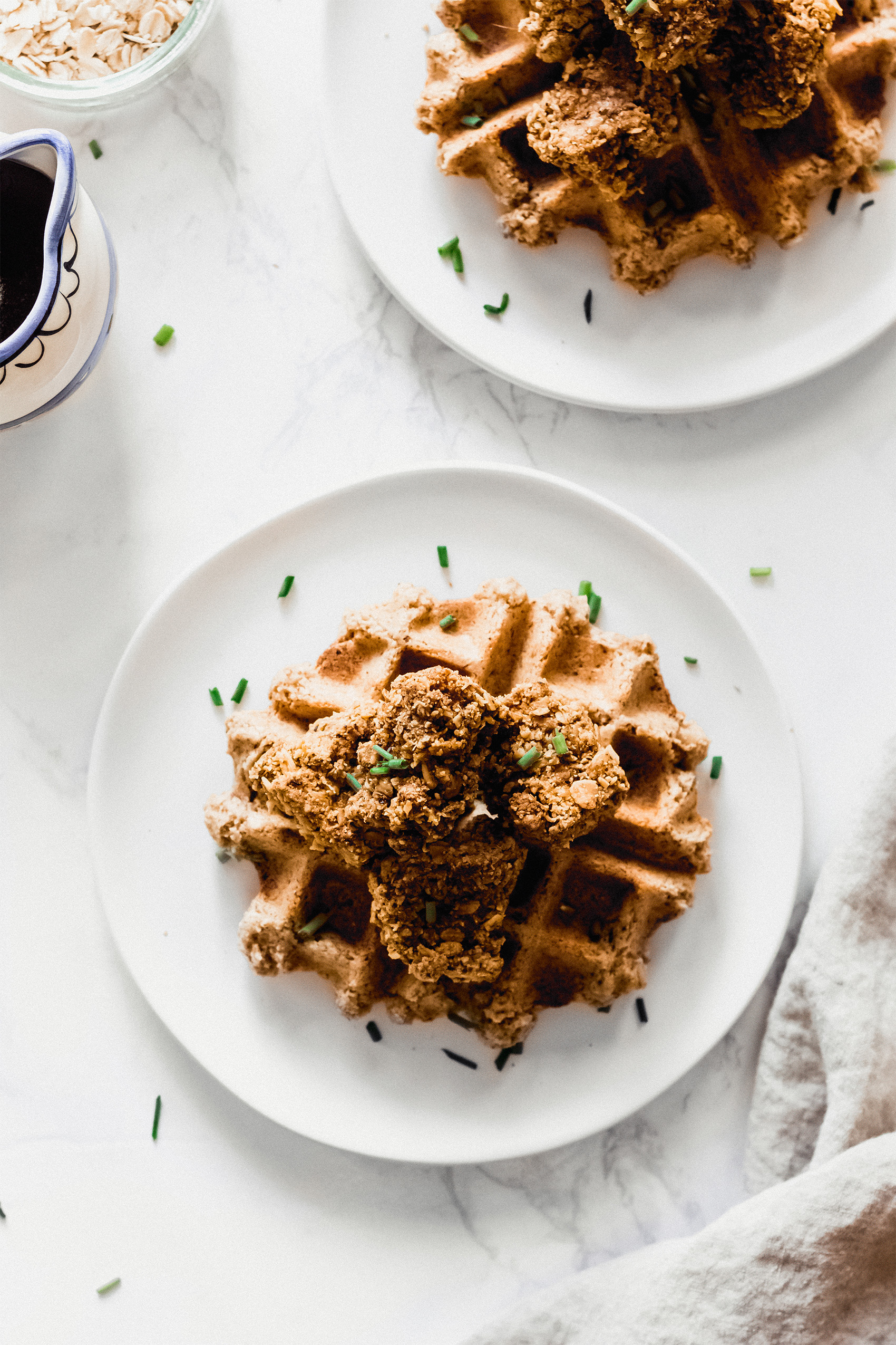 two plates, each with one vegan waffle topped with plant-based fried chicken