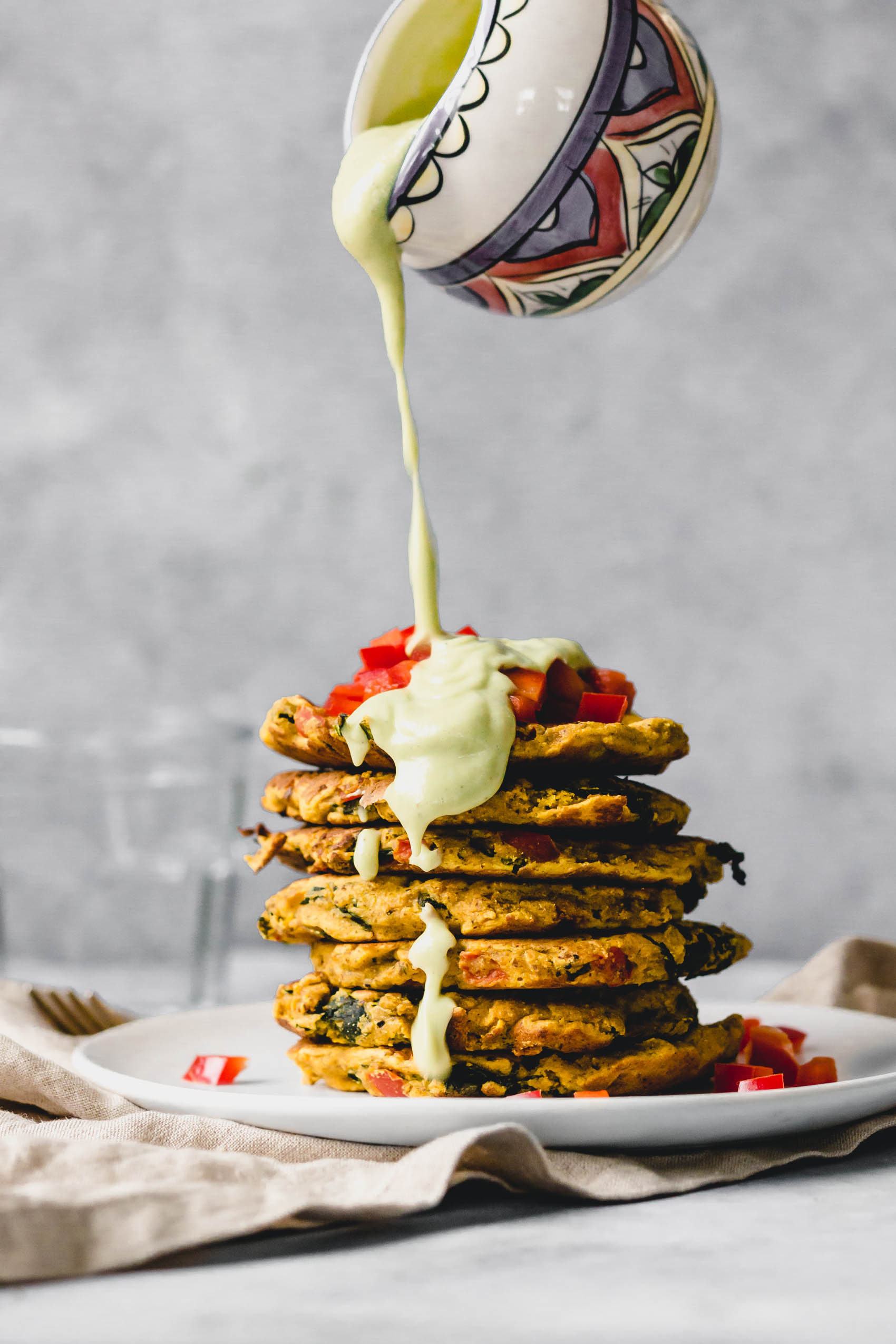 a stack of chickpea pancakes topped with diced tomato and a creamy avocado sauce