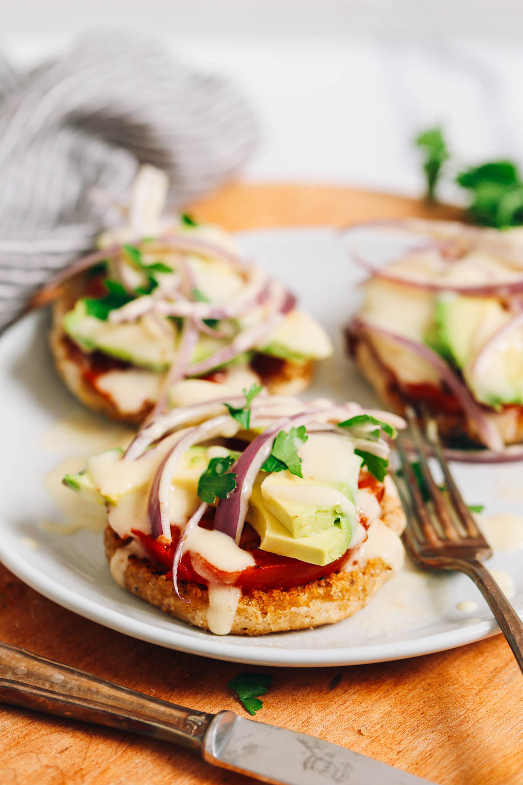 a plate of three vegan eggs benedict servings, each topped with onion, parsley and sliced avocado