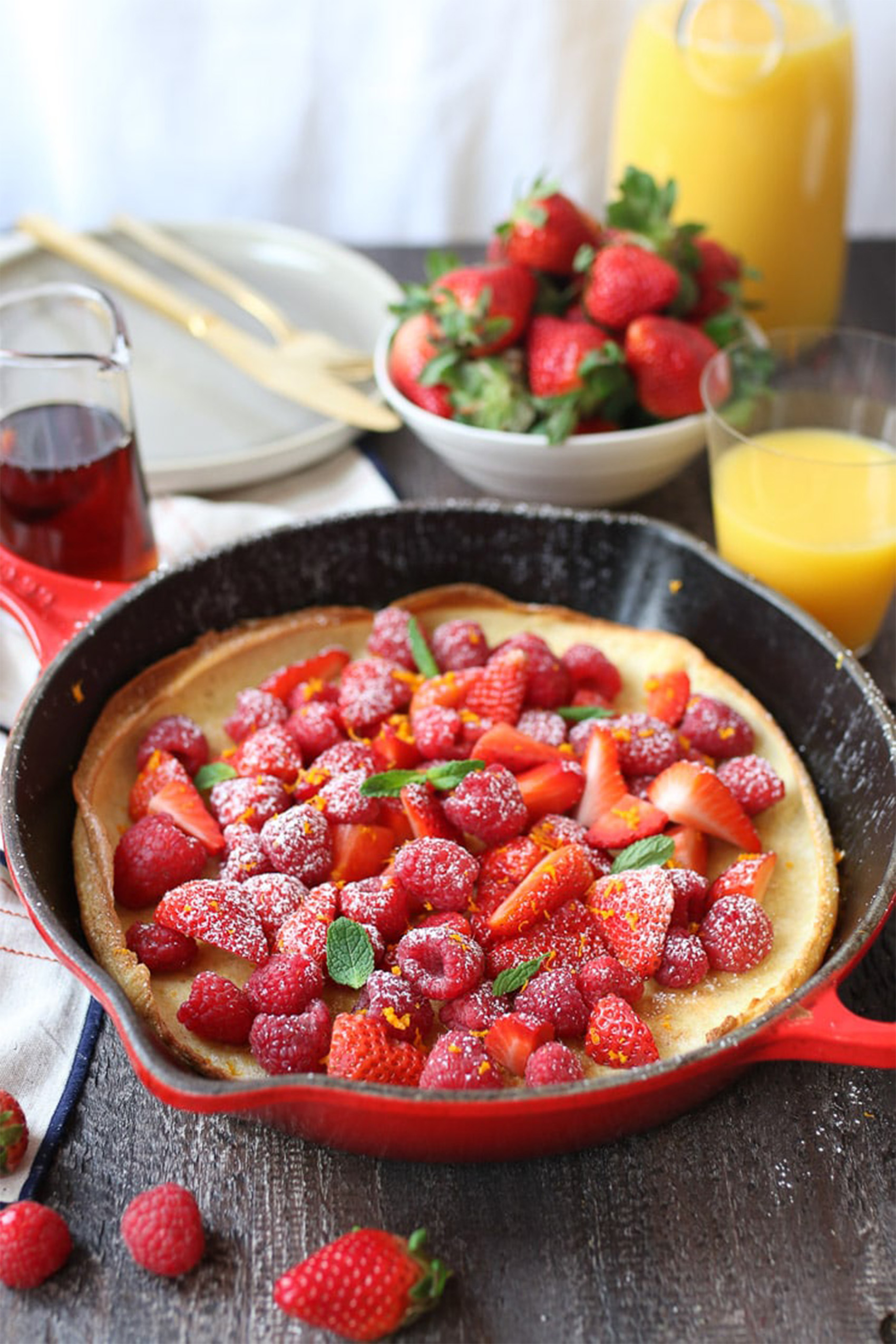 a red cast iron skilled holding a dutch baby topped with berries and mint