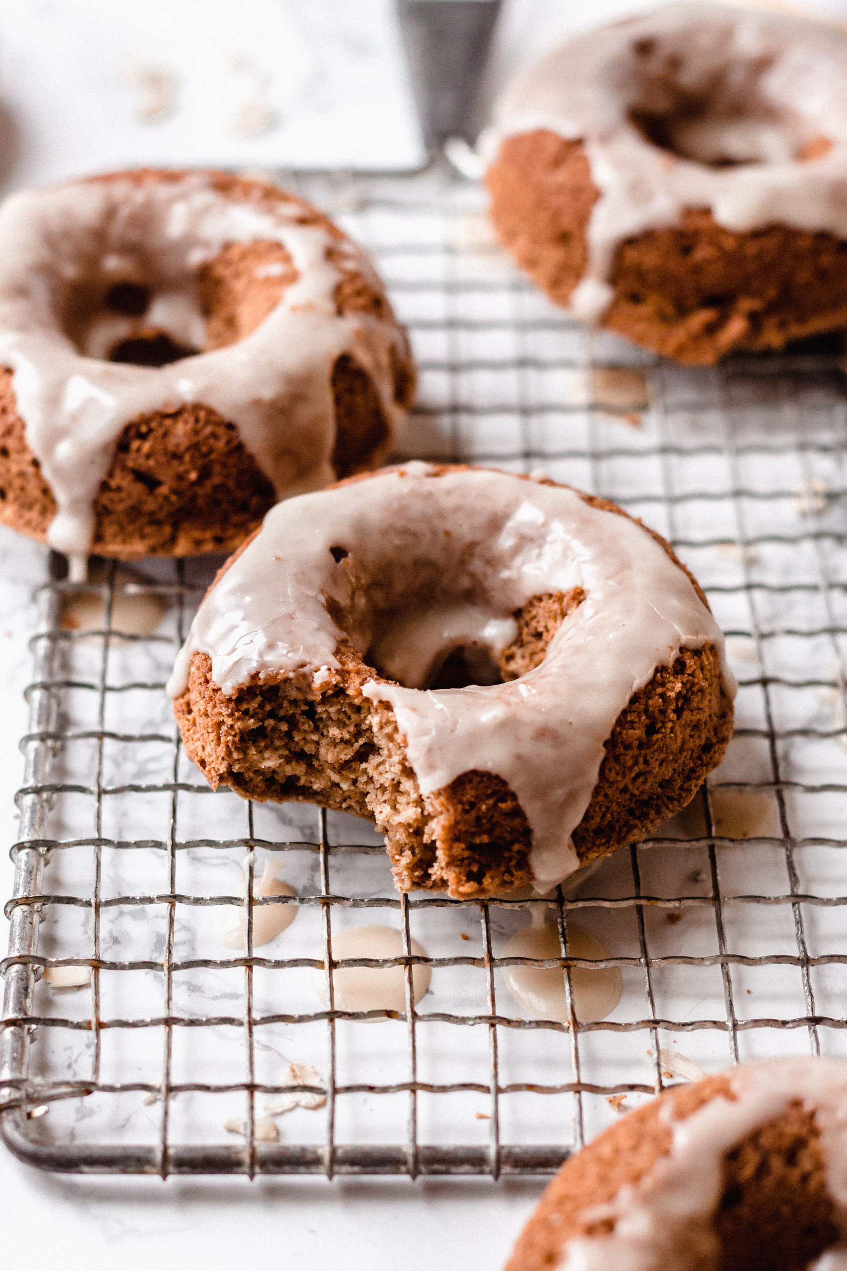 a cooking rack holding three vegan cinnamon donuts topped with a maple glaze