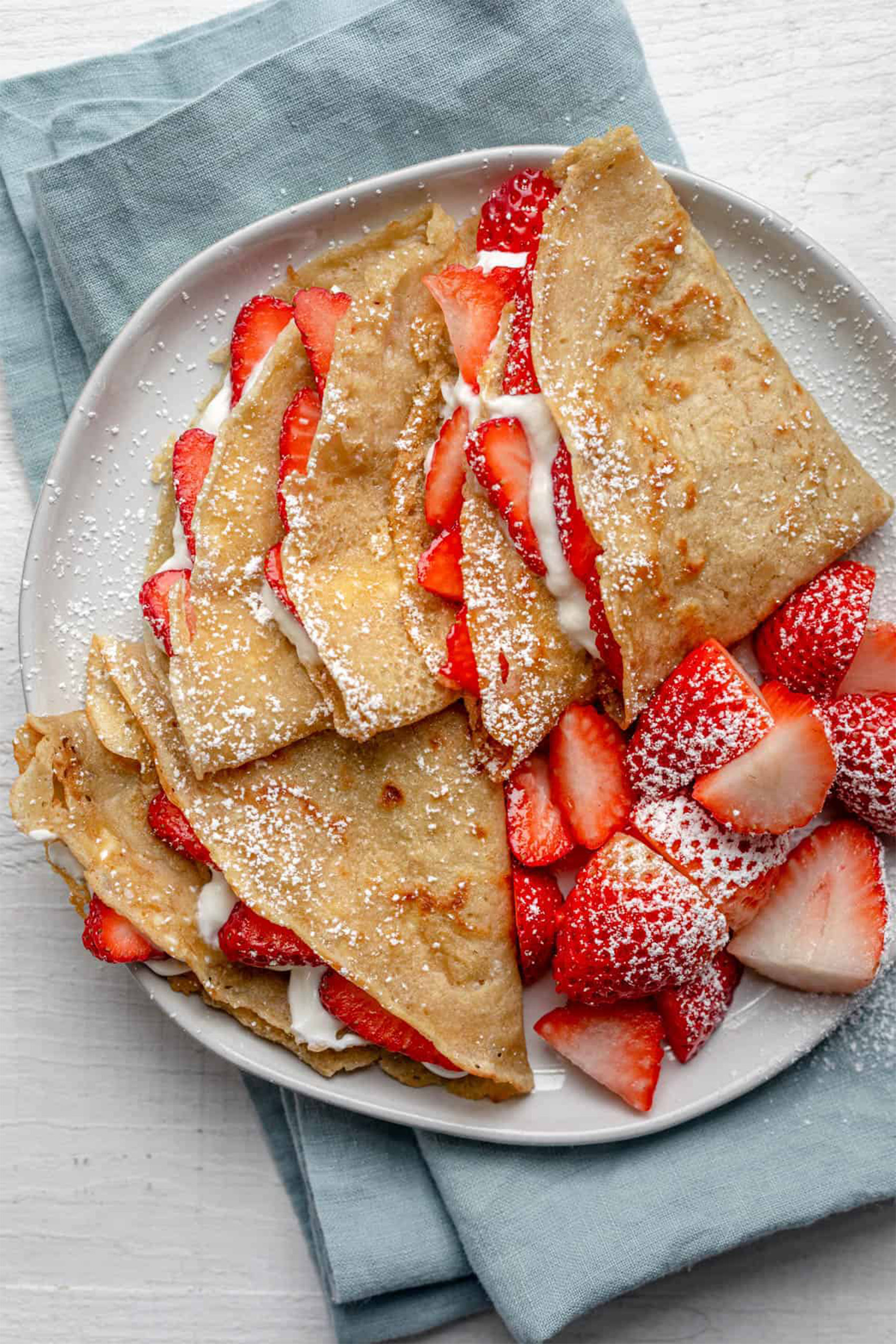 a plate of four folded vegan crepes filled with strawberries and cream filling