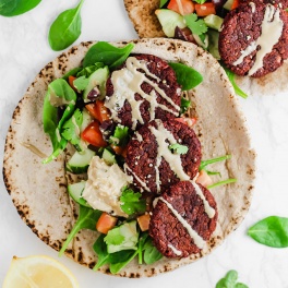 two falafel pitas each topped with a drizzle of tahini and served with lemon wedges
