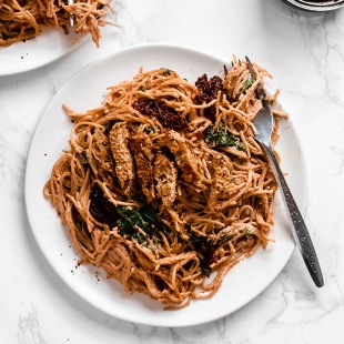 a plate of vegan sun dried tomato spaghetti topped with vegan chicken tenders